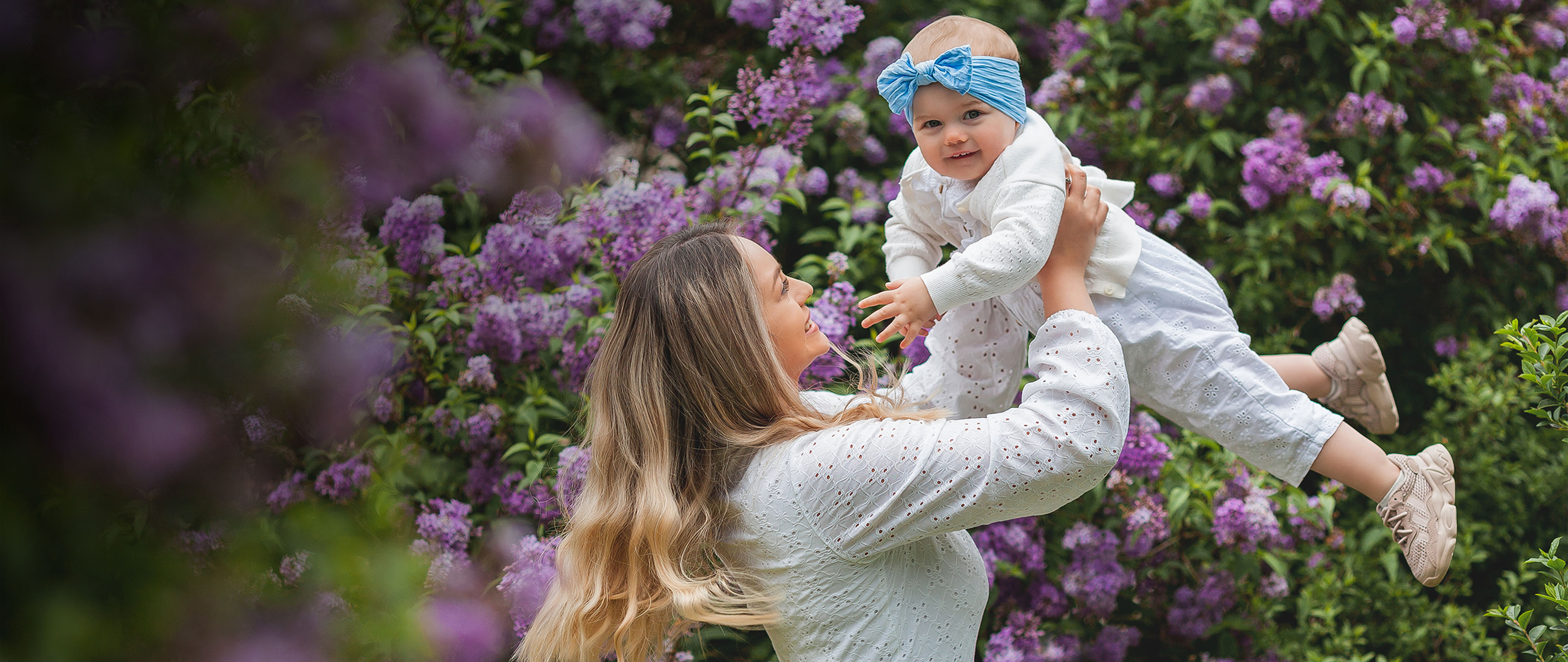 Young beautiful mother with little daughter 1.5 years old in blooming lilacs. Happy family in the park. Spring.